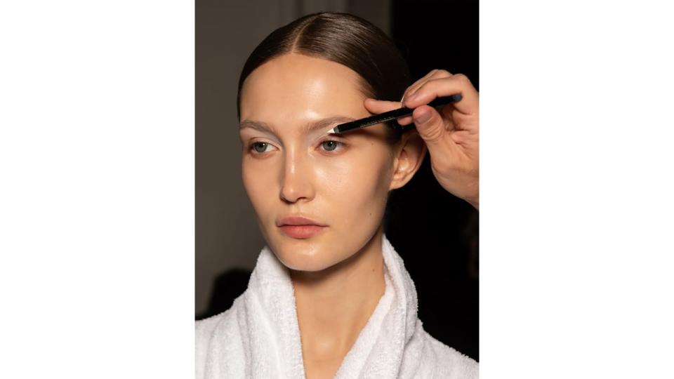 Make up artist Fara Homidi uses a white eyeliner on a model at the Victoria Beckham Autumn/Winter 2024 runway show