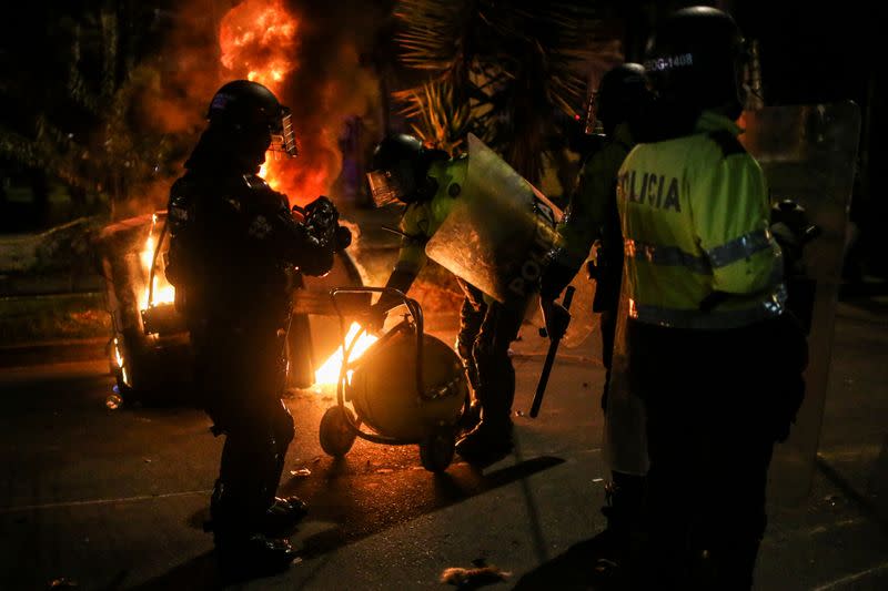 Police officers attempt to extinguish fire from a burning dumpster during a protest after a man, who was detained for violating social distancing rules, died from being repeatedly shocked with a stun gun by officers, according to authorities, in Bogota