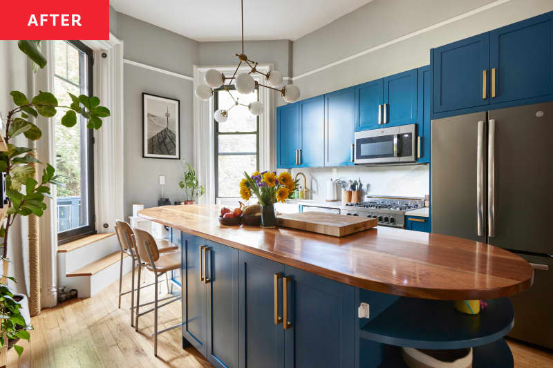 A remodeled grey kitchen with an oval island, blue cabinets and wood-finish countertops.