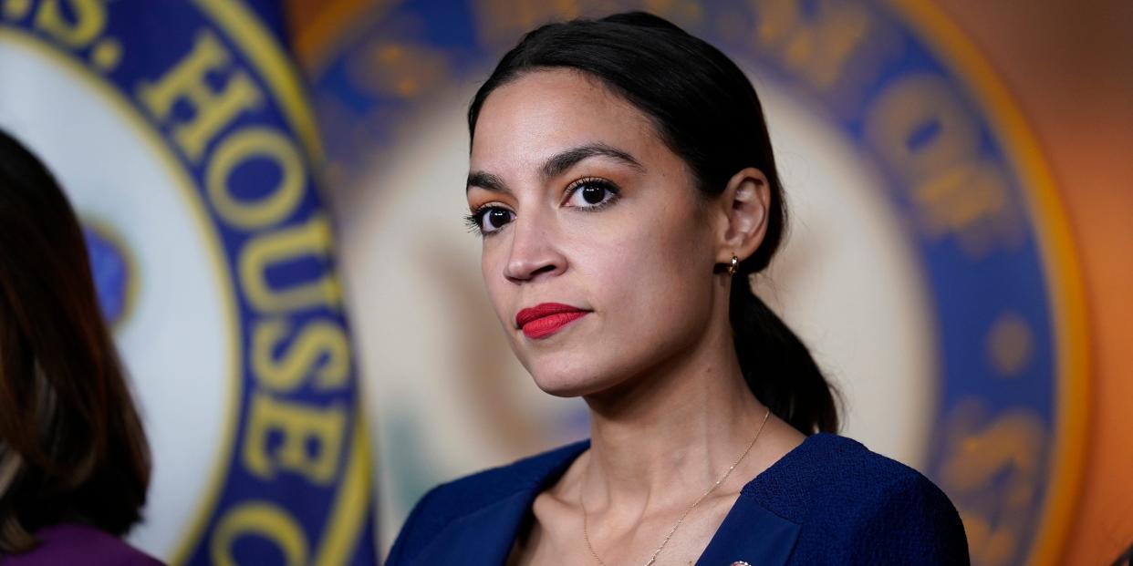 New York Congresswoman Alexandria Ocasio-Cortez in a blue blazer in front of a House of Representatives seal