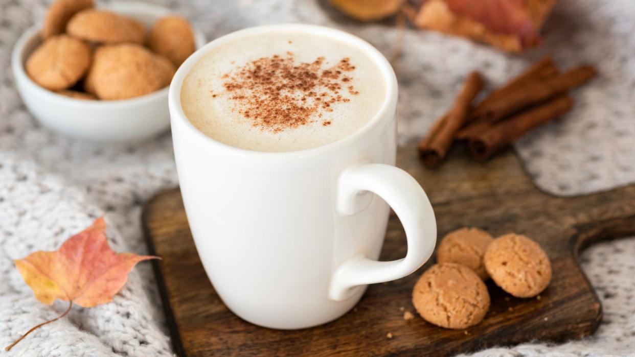  A pumpkin spice latte in a white coffee mug on a board next to biscotti and autumn leaves 