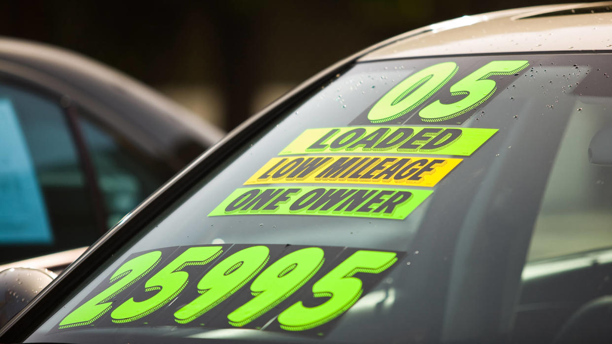 Stickers on the windshield of a car for sale at a used car dealership.