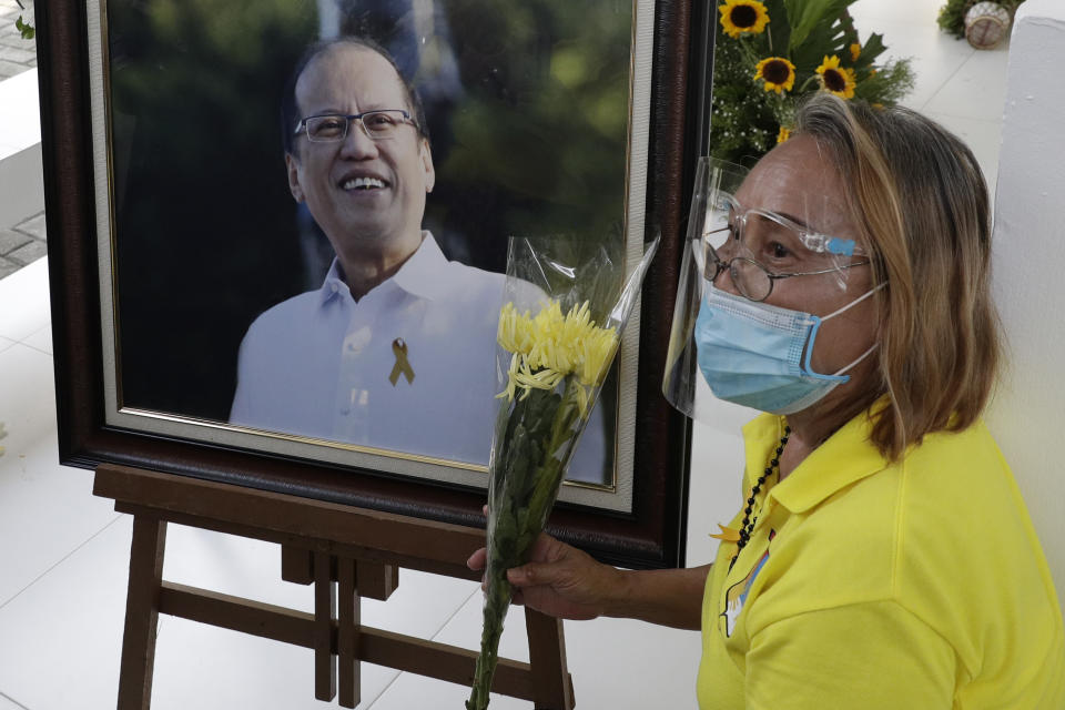 A supporter sits beside a picture of former Philippine President Benigno Aquino III beside his tomb on Saturday, June 26, 2021 at a memorial park in suburban Paranaque city, Philippines. Aquino was buried in austere state rites during the pandemic Saturday with many remembering him for standing up to China over territorial disputes, striking a peace deal with Muslim guerrillas and defending democracy in a Southeast Asian nation where his parents helped topple a dictator. He was 61. (AP Photo/Aaron Favila)