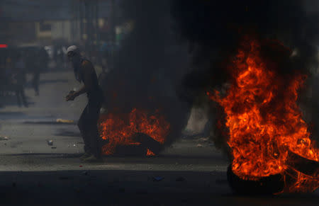 A Palestinian protester stands next to burning tyres during clashes with Israeli troops near Qalandiya checkpoint near the West Bank city of Ramallah July 21, 2017. REUTERS/Mohamad Torokman