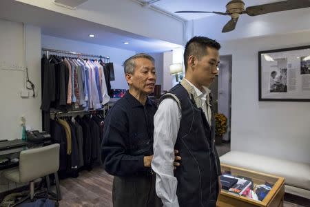 Tailor Cheung Wan-sun (L), 65, checks a customer's new outfit before the final touches, inside a bespoke tailoring firm in Hong Kong February 11, 2015. REUTERS/Tyrone Siu