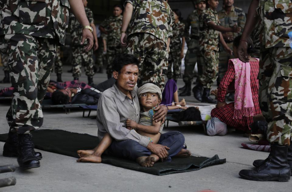 A man sits with a child on his lap as victims of Saturday'ss earthquake, wait for ambulances after being evacuated at the airport in Kathmandu, Nepal, Monday, April 27, 2015.   (AP Photo/Altaf Qadri)
