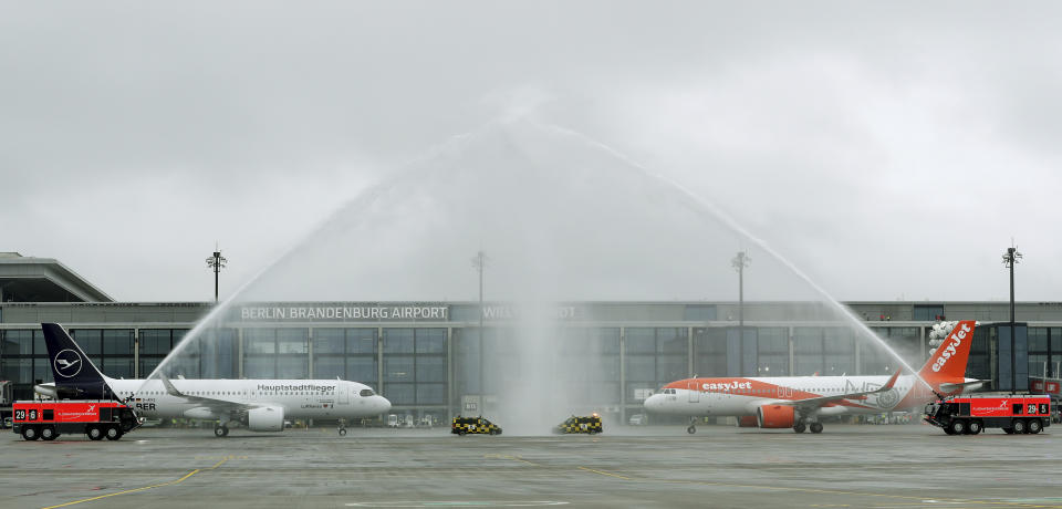 The airport fire brigade sprays water onto a 'Lufthansa', left, and 'easyJet' ariplane that are parked in front of Terminal 1 after their arrival at the new Berlin-Brandenburg-Airport 'Willy Brandt' in Berlin, Germany, Saturday, Oct. 31, 2020. Berlin's new airport opens after years of delays and cost overruns. (AP Photo/Michael Sohn)