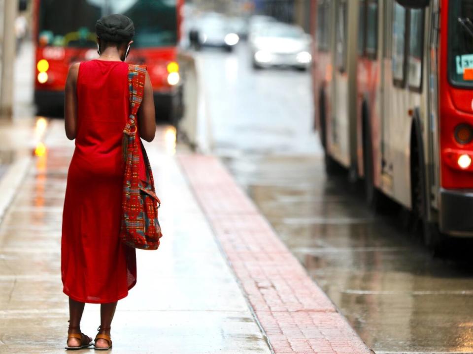 A woman waits for an OC Transpo bus in this file photo. Hundreds of bus trips have been cancelled in recent days, and OC Transpo says the cancellations may continue into next week. (Andrew Lee/CBC - image credit)