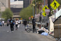 Pedestrians walk along the street next to a homeless encampment as temperatures continue to soar past 115-degrees Thursday, June 17, 2021, in Phoenix. (AP Photo/Ross D. Franklin)