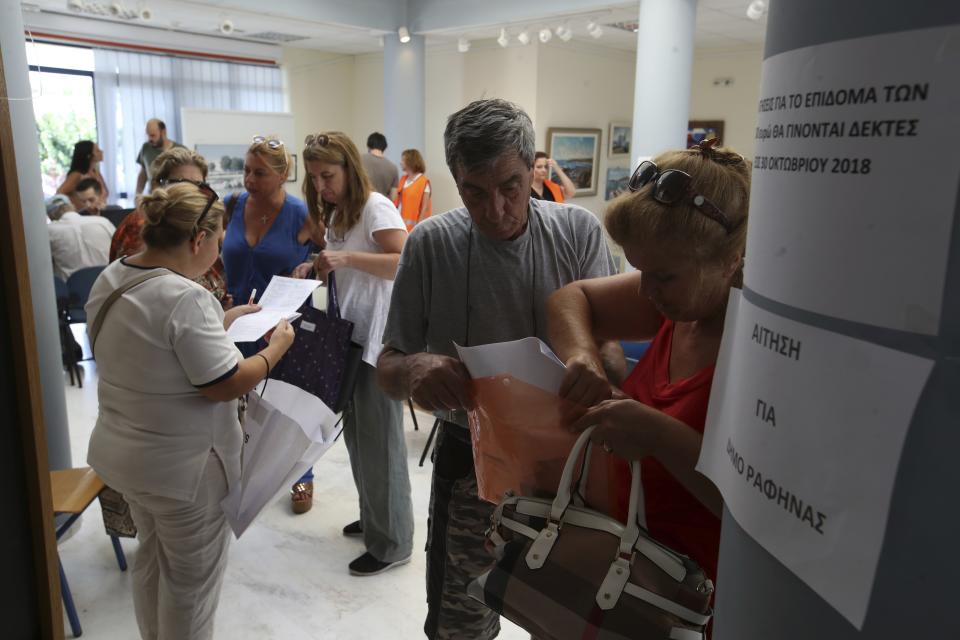 Local residents check their documents as they apply for the 5,000 euro , around $ 5,850 government's financial aid in Rafina, east of Athens, Wednesday, Aug. 1, 2018, ten days after the wildfire. The bodies of 76 people killed by Greece's deadliest wildfire in decades have been identified, authorities said Tuesday, as forensic experts kept working to identify more remains recovered from the charred resort area. Notice reads ‘‘The applications for financial aid will be accepted until Oct. 30, 2018. ’' (AP Photo/Thanassis Stavrakis)