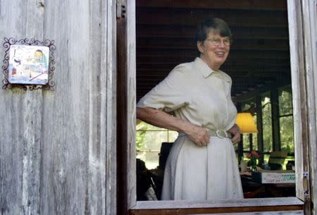 Former U.S. Attorney General Janet Reno greets the media next to a caricature of a journalist and fisherman with the the saying in spanish "A reporter lives here," at the back porch of her home in Miami, September 4, 2001. REUTERS/Colin Braley