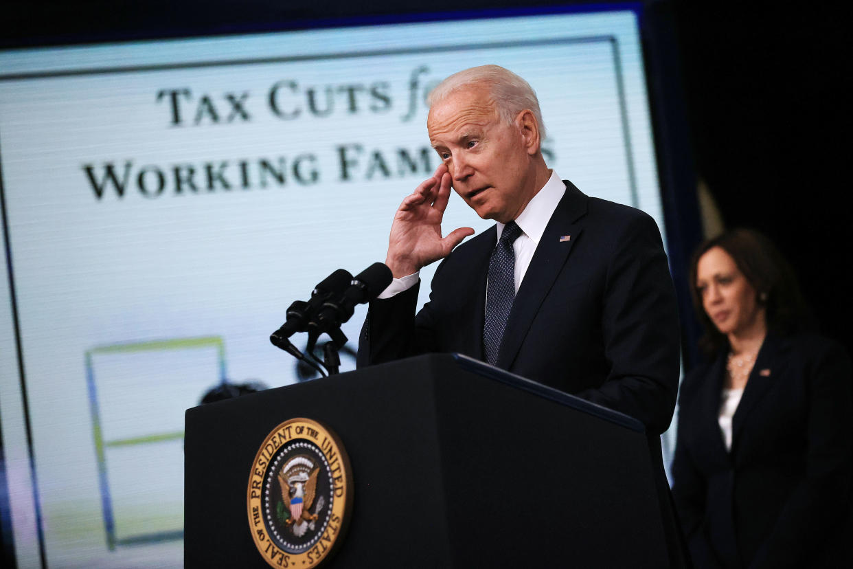 President Biden speaks at a podium on tax cuts with Vice President Kamala Harris standing behind.