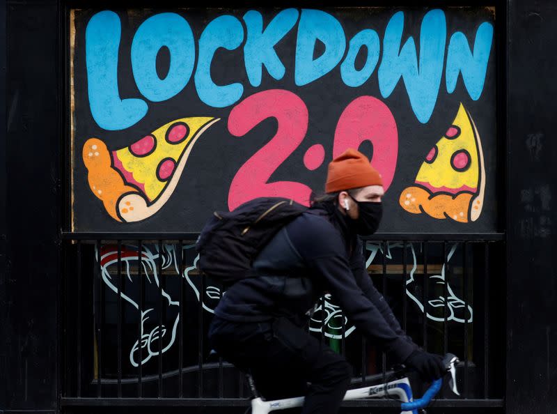 FILE PHOTO: A man cycles past a mural on the boarded up window of a closed pizza restaurant in Manchester