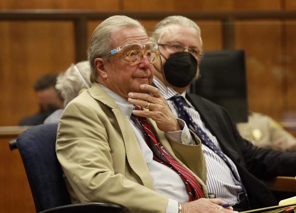 An attorney in a plastic face shield sits next to another attorney in a black mask in court