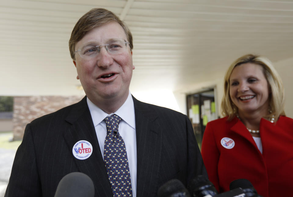 Lt. Gov. Tate Reeves, left, speaks with reporters while his wife Elee Reeves, laughs at his response outside their Flowood, Miss., voting precinct, Tuesday, Nov. 5, 2019. Reeves, the Republican nominee for governor is in one of the state's most hotly contested governor's race since 2003. Voters will also select six other statewide officials and decide on a host of legislative and local offices. (AP Photo/Rogelio V. Solis)