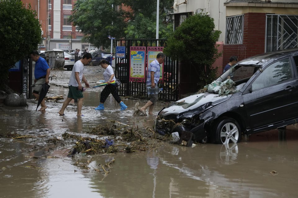 Residents walk near a vehicle damaged and left stranded by flood waters in the Mentougou district on the outskirts of Beijing, Tuesday, Aug. 1, 2023. Chinese state media report some have died and others are missing amid flooding in the mountains surrounding the capital Beijing. (AP Photo/Ng Han Guan)
