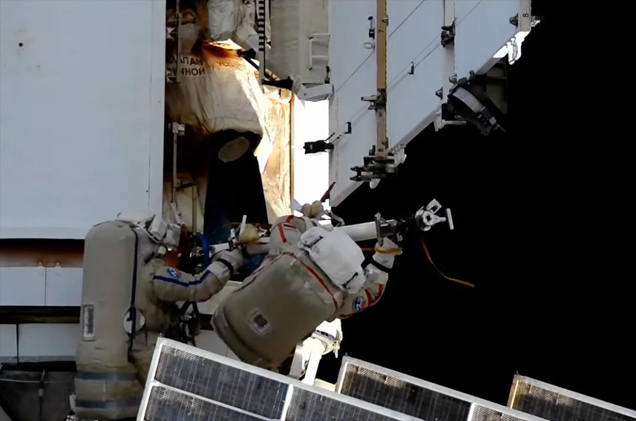  Two cosmonauts wearing white spacesuits conduct a spacewalk outside the international space station. 