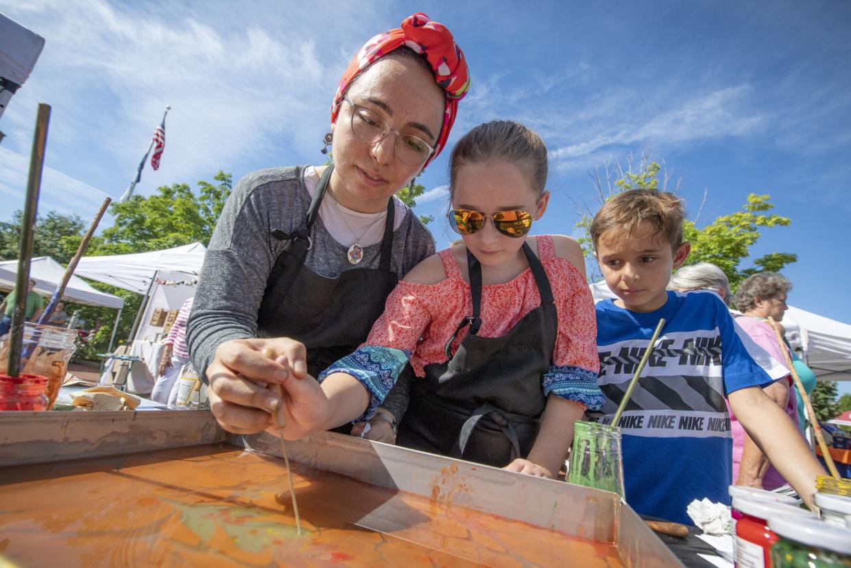 Esra Ibil helps Maggie Ruvalcaba make traditional paper marbling art as Micah Ruvalcaba watches at her booth, Esr’a’rt, during as past A Fair of the Arts.