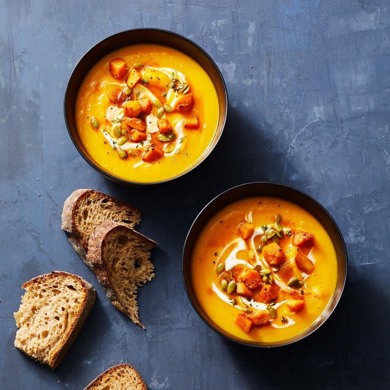 two bowls of butternut squash soup with slices of bread on the side