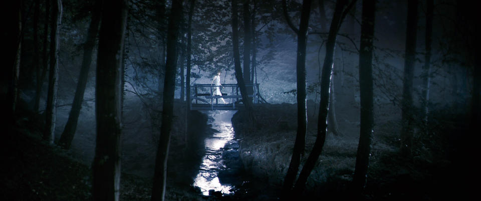 A woman crosses a bridge in the woods