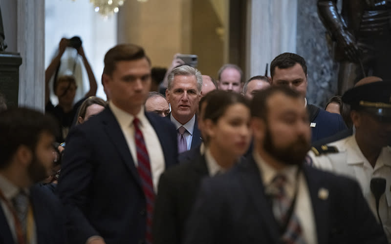Looking down a crowded hallway, Speaker Kevin McCarthy (R-Calif.) walks toward the viewer, surrounded by a crowd of people. A few of the people hold up cameras.