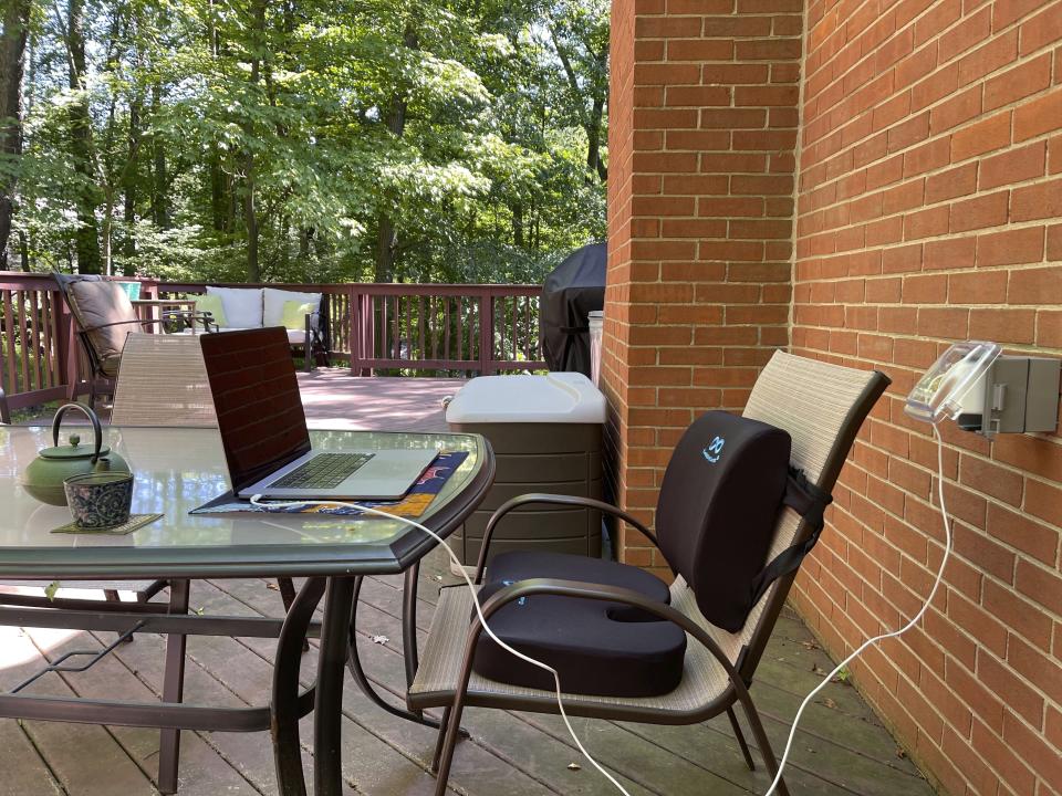 This image provided by Melissa Rayworth shows a lumbar pillow and seat cushion added to an outdoor dining chair to help create a more ergonomic outdoor workspace. Millions of people found themselves working from home during the past year. And many are likely to continue doing so this summer and beyond, even as pandemic restrictions ease. One bonus when working from home: spending some or all of your work day outside. (Melissa Rayworth via AP)