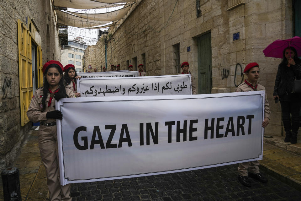 Palestinian scouts hold signs in solidarity with Palestinians in the Gaza Strip calling to end the Israel-Hamas war, near the Church of the Nativity, traditionally believed to be the birthplace of Jesus, on Christmas Eve in the West Bank city of Bethlehem, Sunday, Dec. 24, 2023. Bethlehem is having a subdued Christmas after officials in Jesus' traditional birthplace decided to forgo celebrations due to the Israel-Hamas war. (AP Photo/Mahmoud Illean)