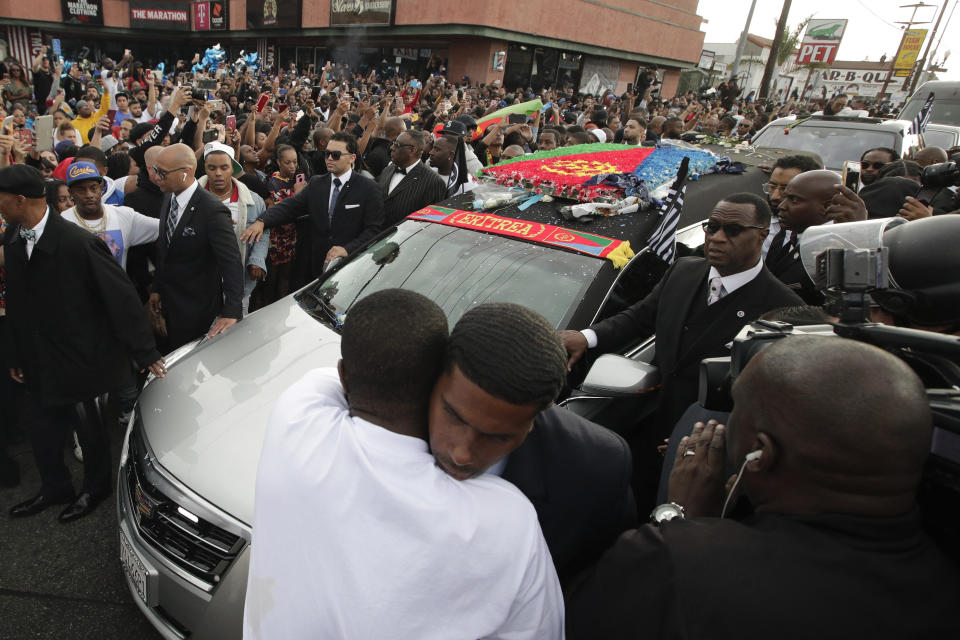 Two men hug as a hearse carrying the casket of slain rapper Nipsey Hussle passes through the crowd Thursday, April 11, 2019, in Los Angeles. The 25-mile procession traveled through the streets of South Los Angeles after his memorial service, including a trip past Hussle's clothing store, The Marathon, where he was gunned down March 31. (AP Photo/Jae C. Hong)