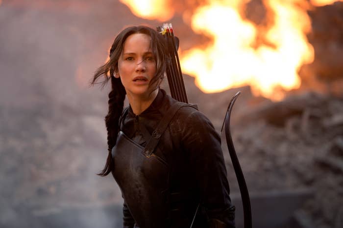 Jennifer Lawrence as Katniss Everdeen in "The Hunger Games: Mockingjay Part 2," wearing battle gear with bow and arrows, stands in front of an explosion