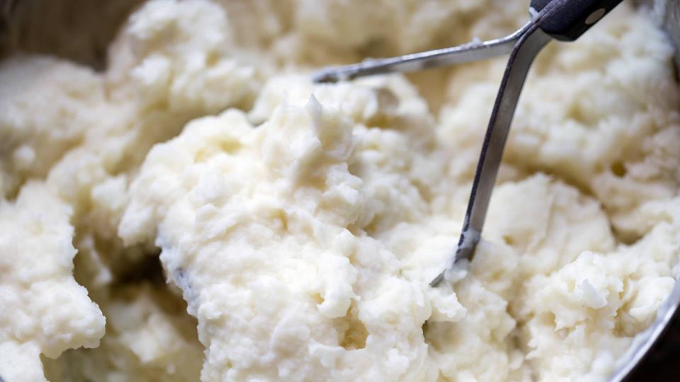 Close-up of mashed potatoes and potato masher in a kettle.