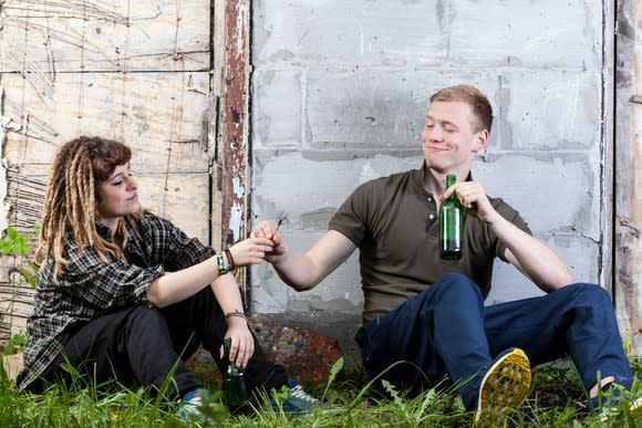 A man and woman sharing beer and marijuana outside.