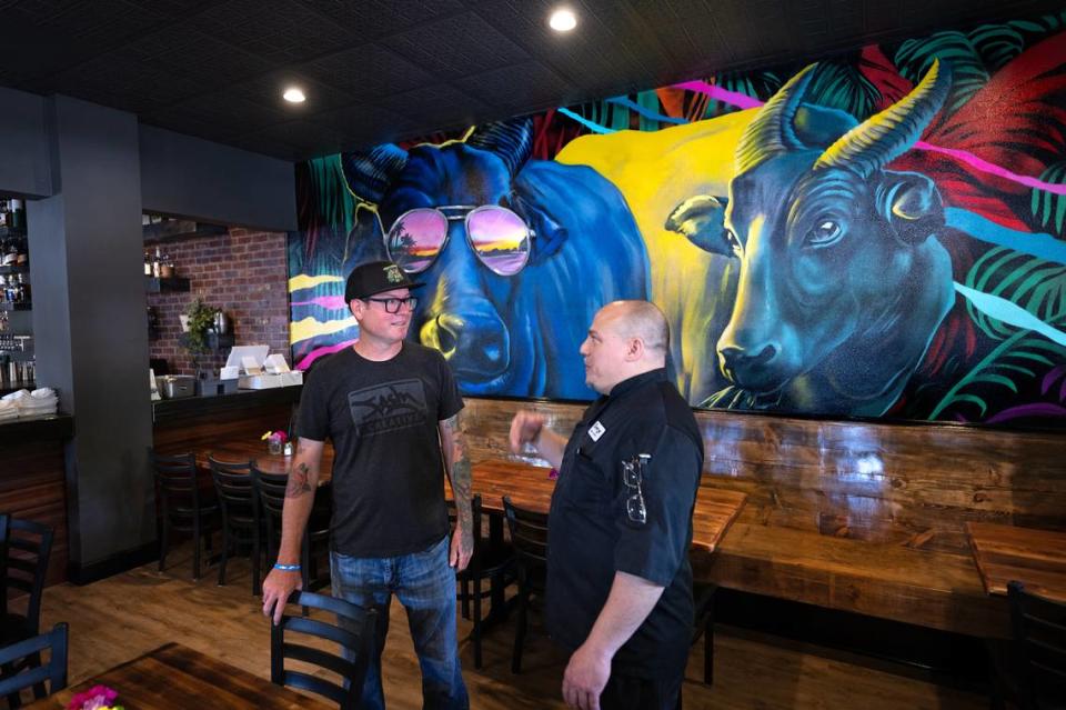 El propietario y chef George Bertaina habla con el artista FASM, el alias de Aaron Vickery, en el restaurante Cora en Roseburg Square en Modesto, California, el viernes 24 de mayo de 2024. FASM pintó el mural en la pared del comedor.