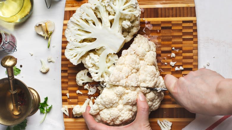 Hand cutting cauliflower on cutting board 