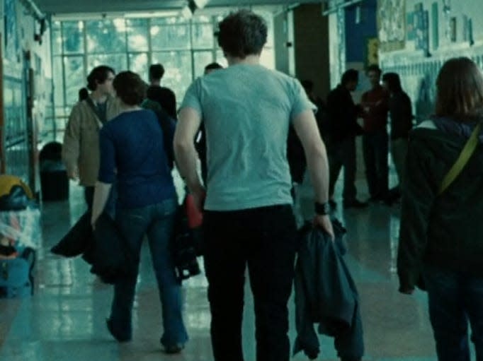 Edward walking away down a crowded hallway with other students in twilight