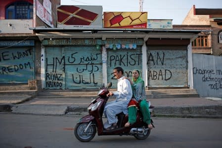 Kashmiris ride on a scooter past the closed shops painted with graffiti during restrictions, in Srinagar