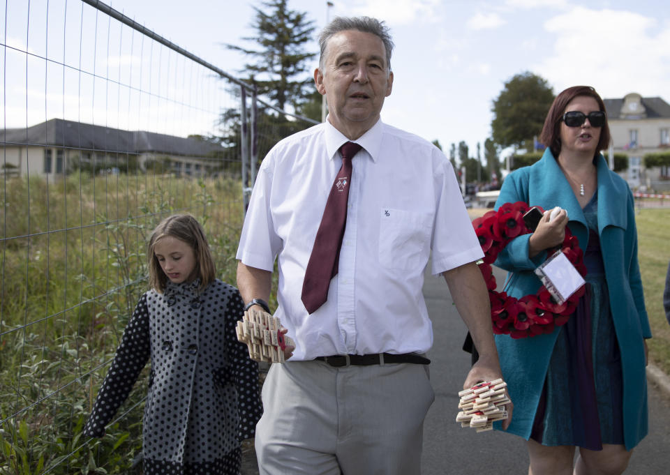 British expatriate Steven Oldrid, center, carries wooden crosses with names of WWII dead as he walks to the local war cemetery in Benouville, Normandy, France on Saturday, June 6, 2020. Due to coronavirus measures many relatives and veterans will not make this years 76th anniversary of D-Day. Oldrid will be bringing it to them virtually as he places wreaths and crosses for families and posts the moments on his facebook page. (AP Photo/Virginia Mayo)