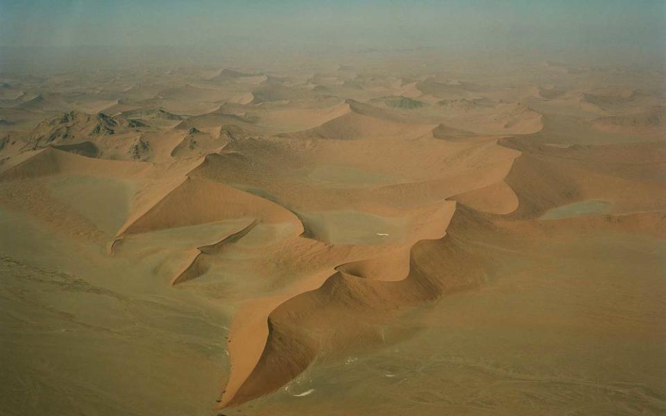 An aerial view of Sossusvlei, a region of the Namib Desert known for its towering sand dunes, which are among the highest in the world. The iconic, 280-foot-high Dune 45 is visible at the bottom of the image.