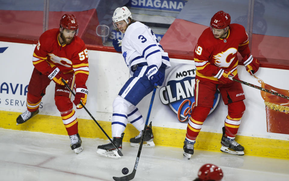 Toronto Maple Leafs' Justin Holl, centre, plays the puck in between Calgary Flames' Noah Hanifin, left, and Matthew Tkachuk during the second period of an NHL hockey game, Tuesday, Jan. 26, 2021 in Calgary, Alberta. (Jeff McIntosh/The Canadian Press via AP)