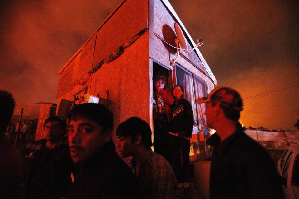 People gather at a street corner as the scene is illuminated by the glow of encroaching forest fires in Valparaiso, Chile, Sunday April 13, 2014. Authorities say the fires have destroyed hundreds of homes, forced the evacuation of thousands and claimed the lives of at least seven people. ( AP Photo/ Luis Hidalgo)