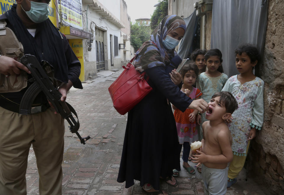 A police officer stand guard while a health worker administers a polio vaccine to a child in Peshawar, Pakistan, Friday, July 30, 2021. The Pakistani government launched an anti-polio vaccination campaign in an effort to eradicate the crippling disease. (AP Photo/Muhammad Sajjad)