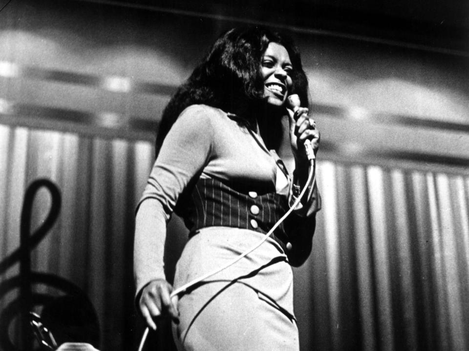 Lyn Collins, holding a microphone and performing on stage.