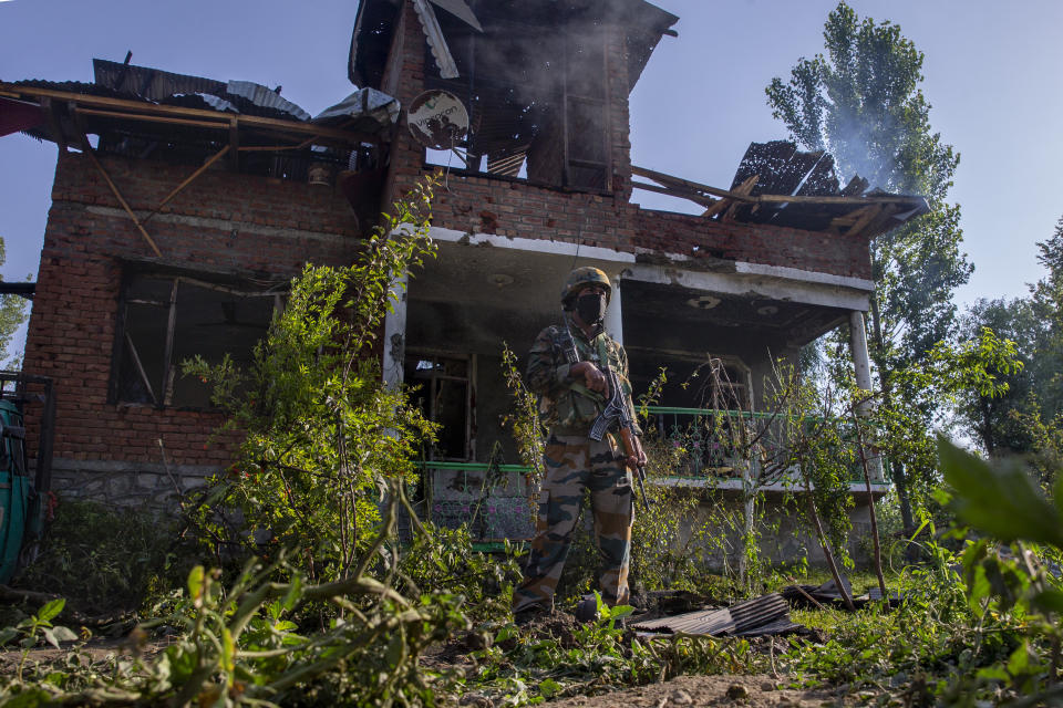 An Indian army soldier stands guard as colleagues check for explosives inside a house damaged in a gun battle in the outskirts of Srinagar, Indian controlled Kashmir, Tuesday, June 29, 2021. Hours after arresting a rebel commander, police Tuesday said he was killed during a crossfire with another militant in the disputed city's region's main city. (AP Photo/Dar Yasin)