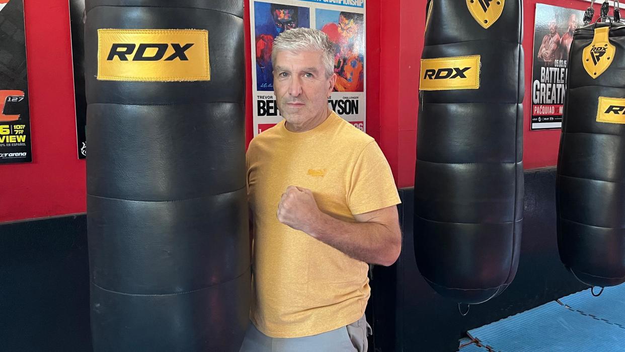 Steve Kerridge poses next to a punching bag with his fist raised. He is wearing a yellow T-shirt and looking directly at the camera. 