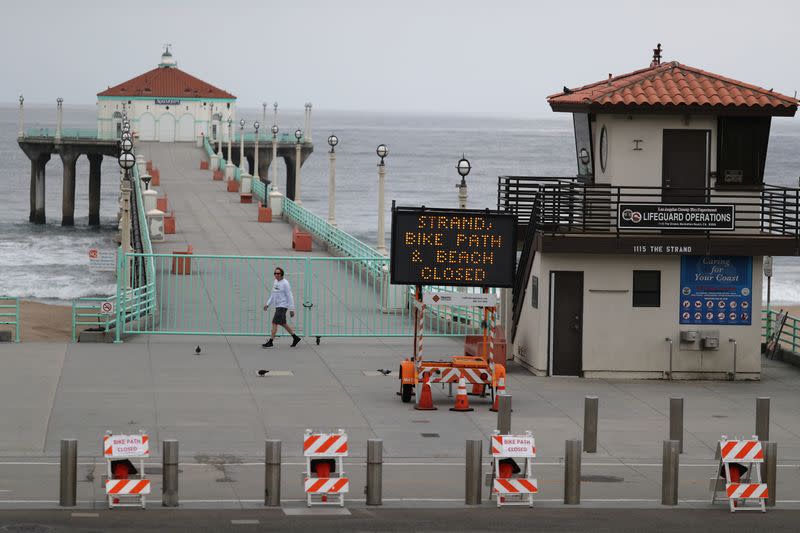 A man walks near the gate on the closed Manhattan Beach Pier after Los Angeles issued a stay-at-home order and closed beaches and state parks, as the spread of the coronavirus disease (COVID-19) continues, in Manhattan Beach