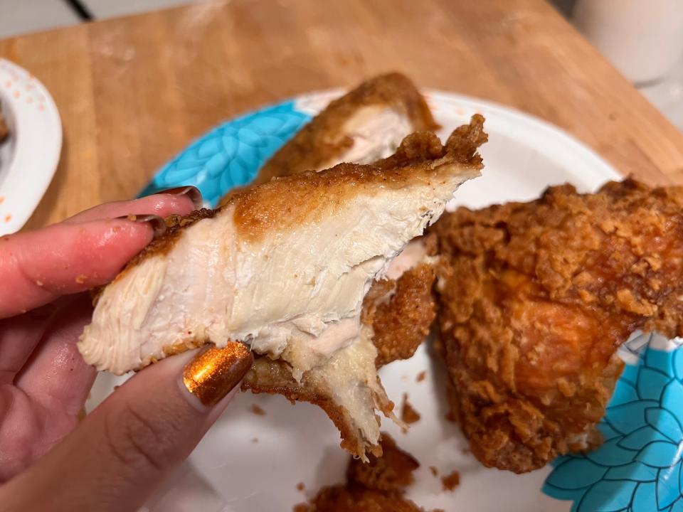 Hand holding piece of Lucky's fried chicken in front of white and blue plate