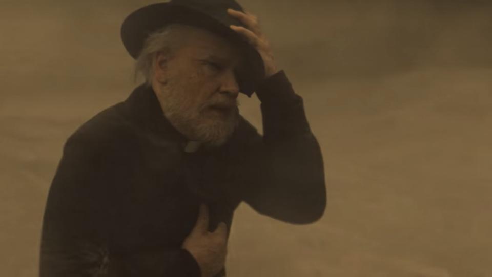 Monsignor Pruitt protects himself from a sand storm in the desert on Midnight Mass