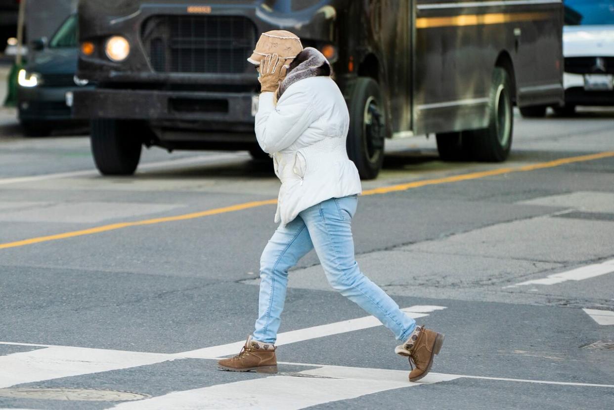 A woman holds onto her hat as she crosses an intersection near Toronto's Front Street. (Sam Nar/CBC - image credit)