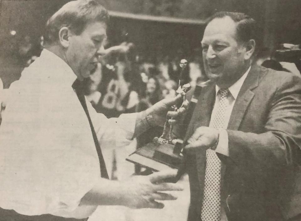 Milbank girls baskeball coach Gordie Bergquist (left) receives the state championship trophy from Dr. Iro Mogen of the S.D. High School Activities Association's board of contral after the Bulldogs defeated Lennox 56-44 in the 1987 state Class A girls basketball championship at Mitchell's Corn Palace.