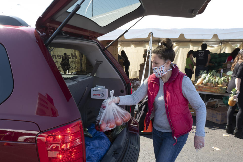 A volunteer places a bag of tomatoes into a slowly moving vehicle at a Foodshare distribution center at Rentschler Field in East Hartford, Conn., May 7, 2020, during the coronavirus pandemic. (AP Photo/Mark Lennihan)