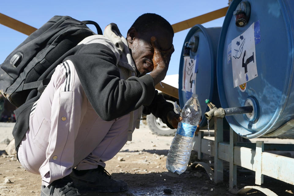 A man from Kenya washes his face and fill his water bottle as hundreds of migrants gather along the border Tuesday, Dec. 5, 2023, in Lukeville, Ariz. The U.S. Border Patrol says it is overwhelmed by a shift in human smuggling routes, with hundreds of migrants from faraway countries like Senegal, Bangladesh and China being dropped in the remote desert area in Arizona. (AP Photo/Ross D. Franklin)